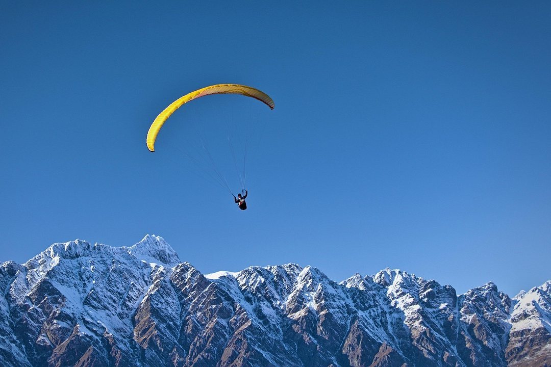 Parachute canopy flying above snow-capped mountains under a clear blue sky