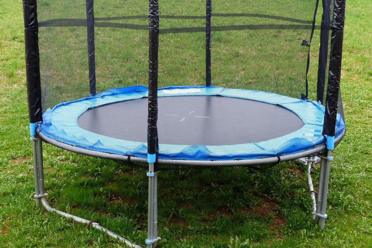 A backyard trampoline with a safety net on a lawn