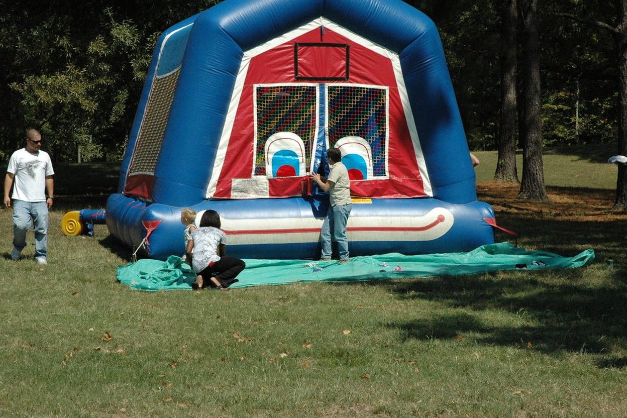 People setting up a red, white, and blue bounce house in a grassy park.