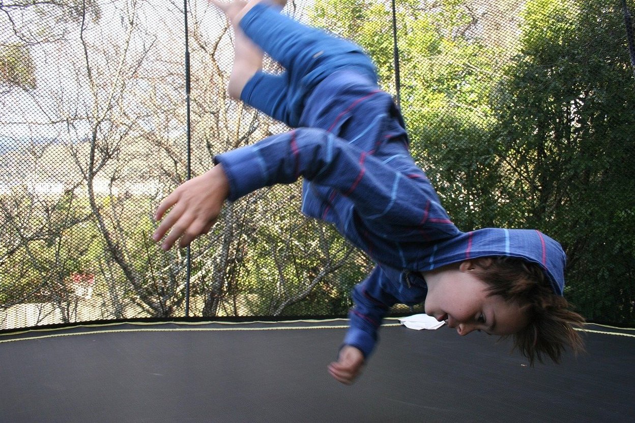 A backyard trampoline with a safety net and protective padding in a residential yard