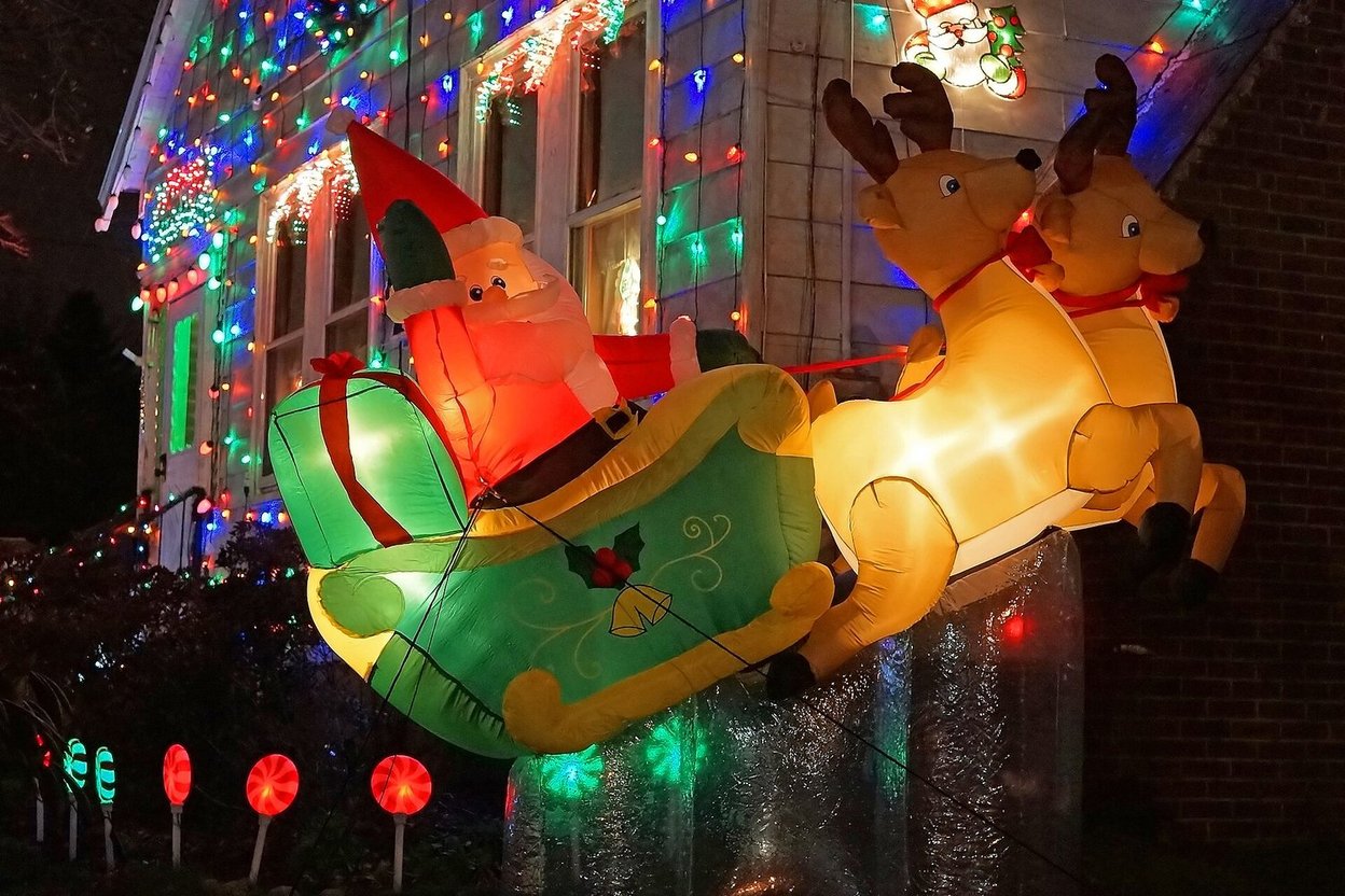 Inflatable Santa in sleigh pulled by reindeer, glowing with Christmas lights on a house.