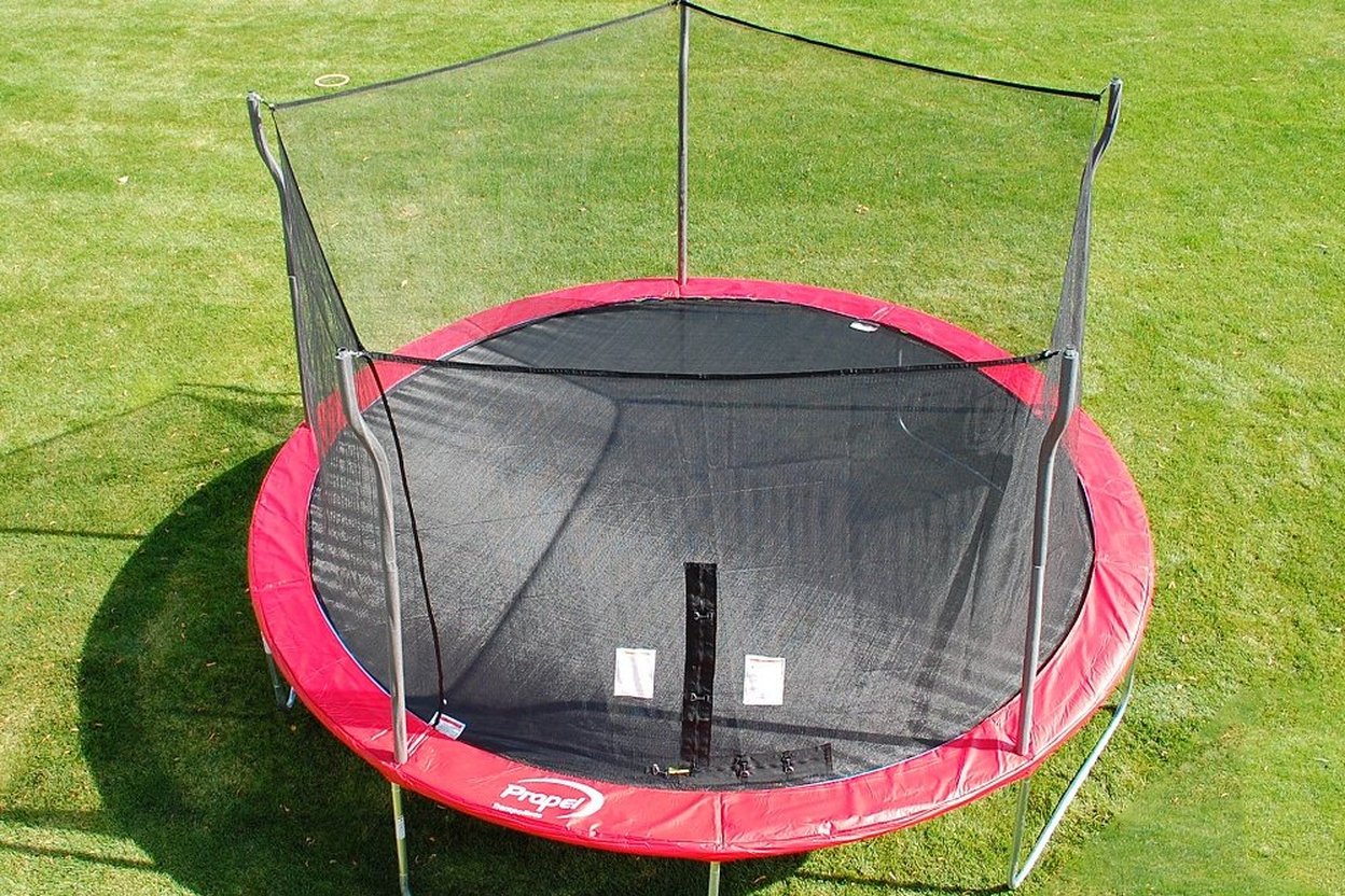 A round backyard trampoline with a safety net enclosure on a green lawn
