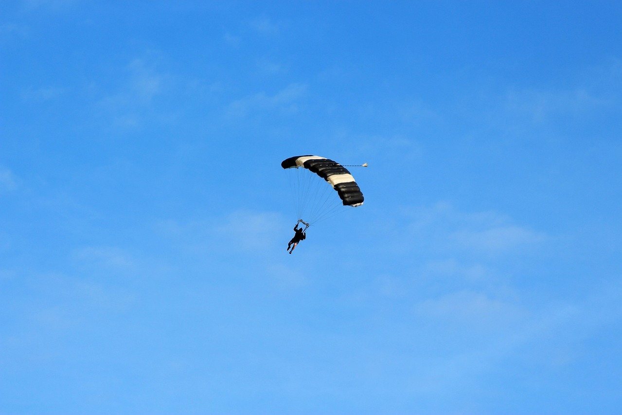 Parachutist descending with black and white canopy against clear blue sky