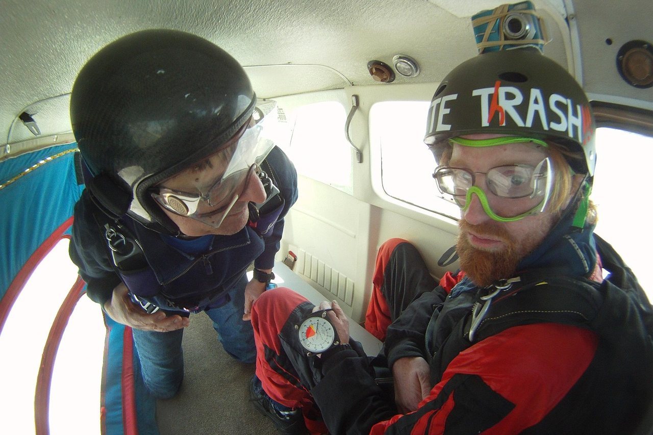 Two skydivers in a plane, checking equipment before jumping