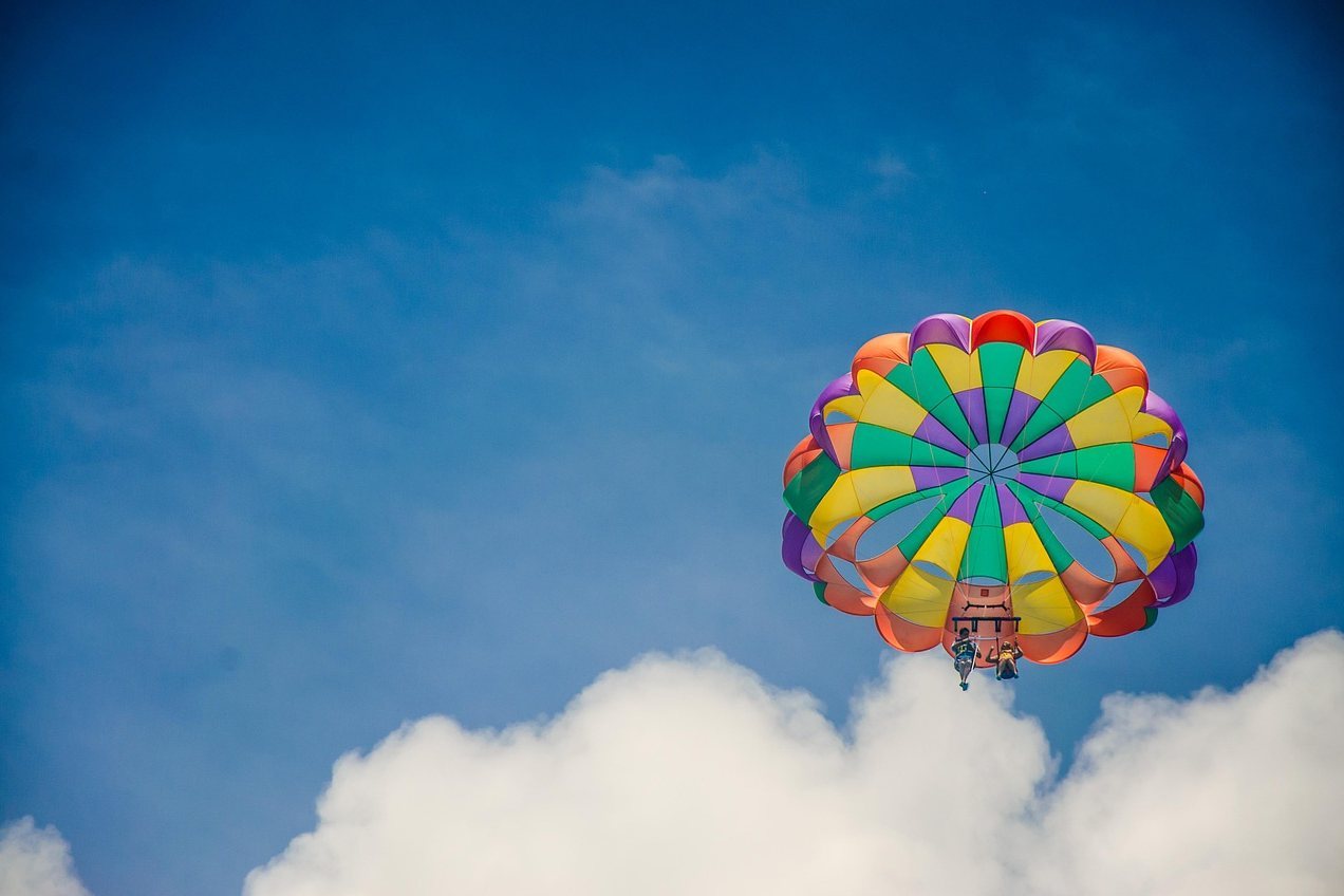 Colorful parachute canopy flying above white clouds against a blue sky