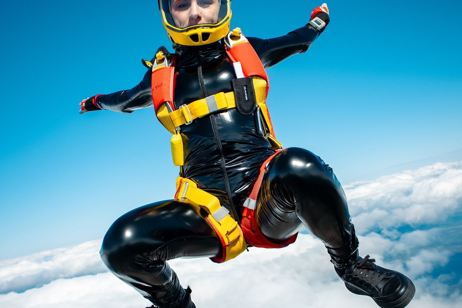 Skydiver in black suit and yellow helmet mid-air above clouds
