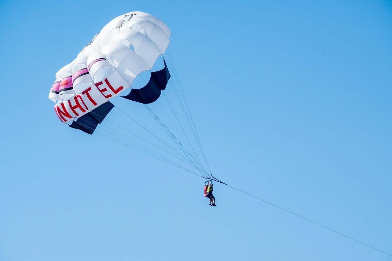 Person flying under a parachute against a clear blue sky