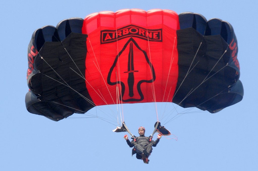 Parachutist under a red and black Airborne parachute against a blue sky