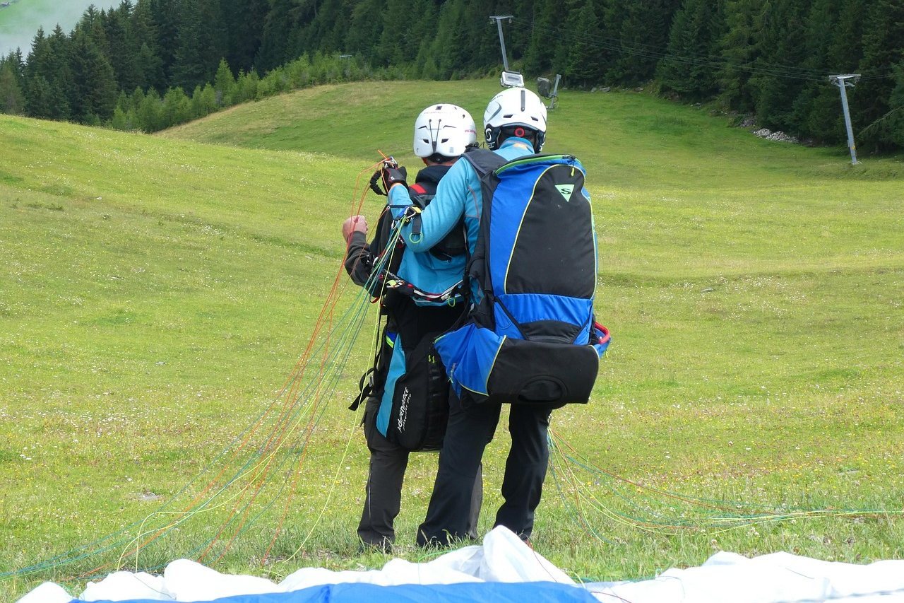 Two people readying a tandem canopy on a grassy hillside with forest behind