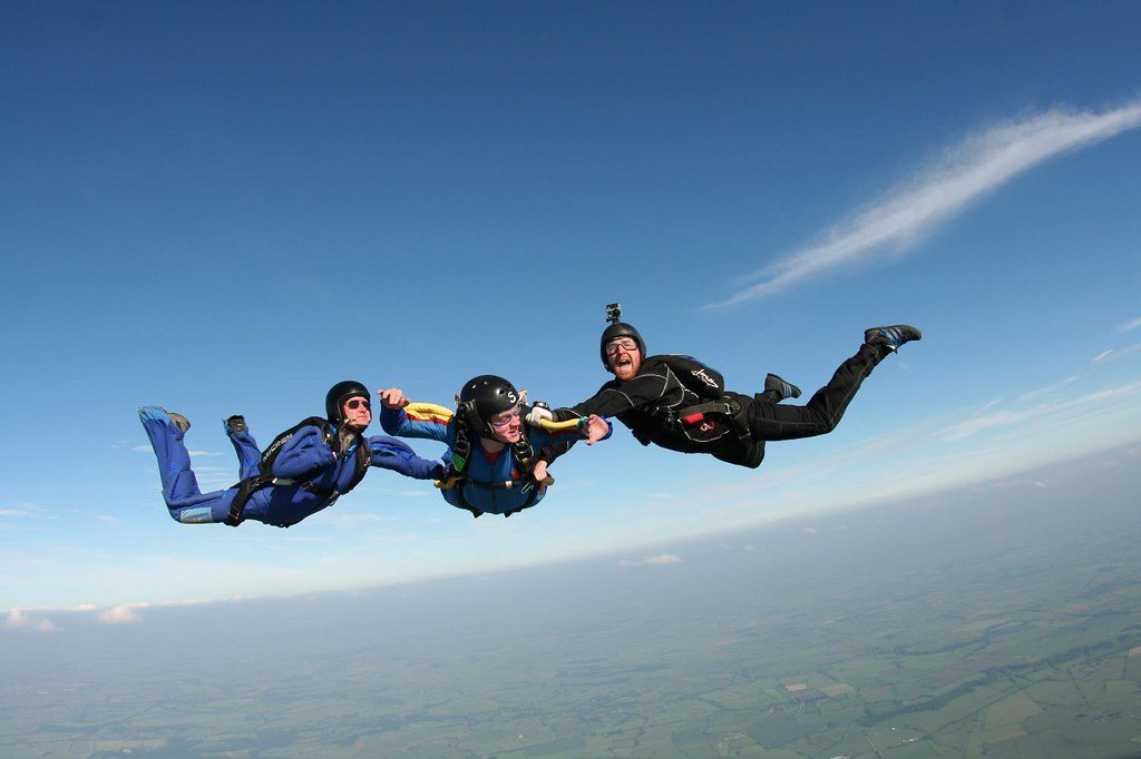 Three skydivers in freefall against a clear blue sky with earth below
