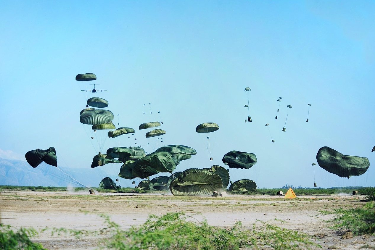 Paratroopers descending with green parachutes during a military training exercise