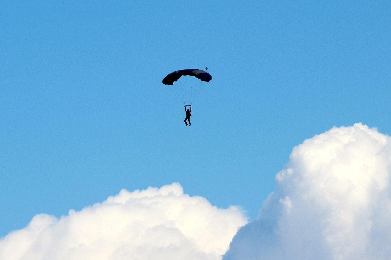 Parachutist descending with open parachute against blue sky and white clouds