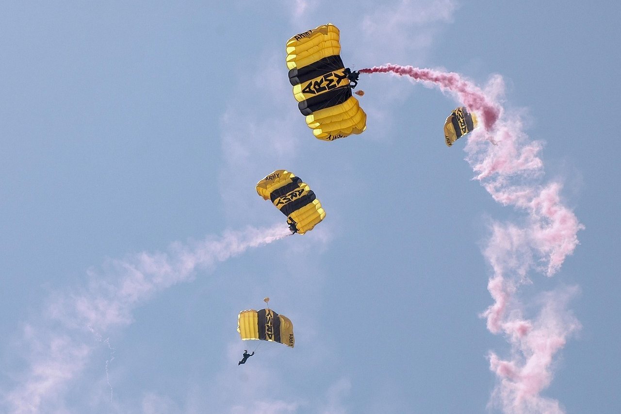 Parachutists with yellow and black canopies trailing pink smoke in formation