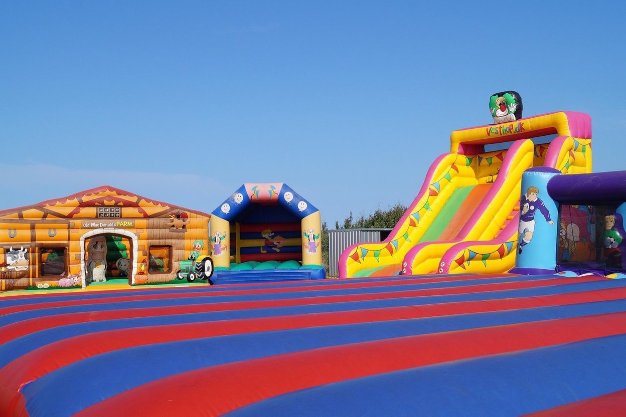 Children jumping on a large bounce house with a slide at a backyard birthday party, with a blower and extension cord visible on the grass.