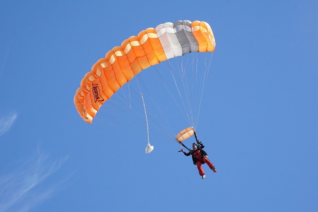 Parachutist in orange and white canopy descending against clear blue sky