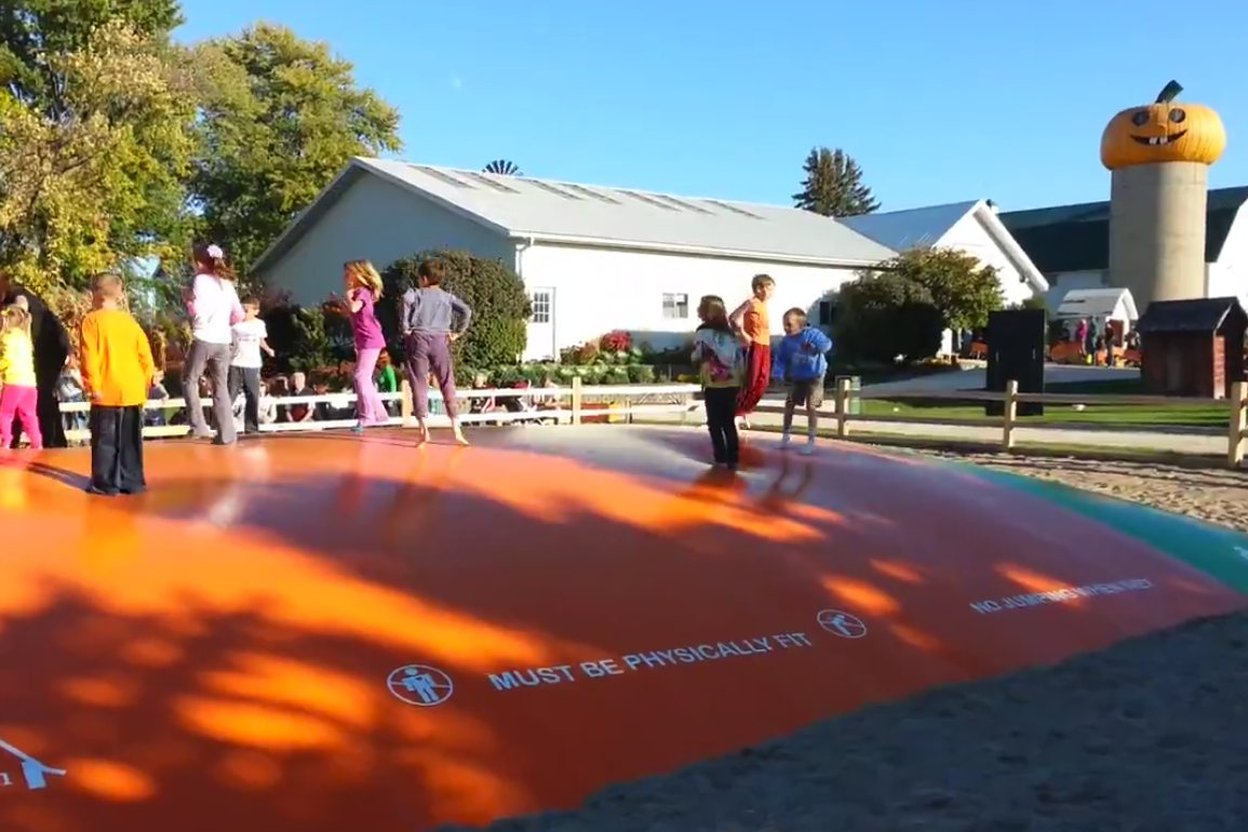 An inflatable bounce house set up at a pumpkin patch, with anchor stakes visible in the ground and the blower equipment positioned nearby.