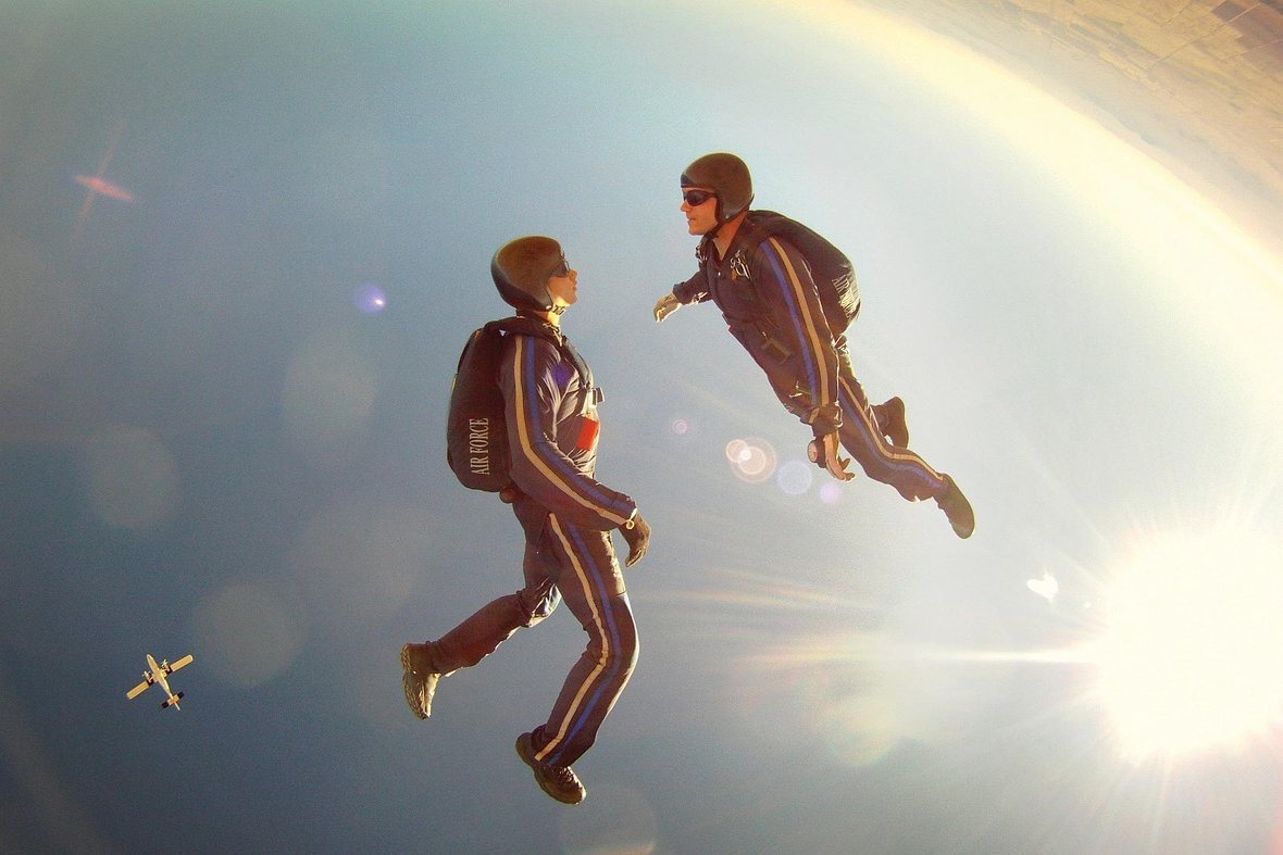 Two skydivers in flight suits freefalling toward Earth with a small plane in the distance