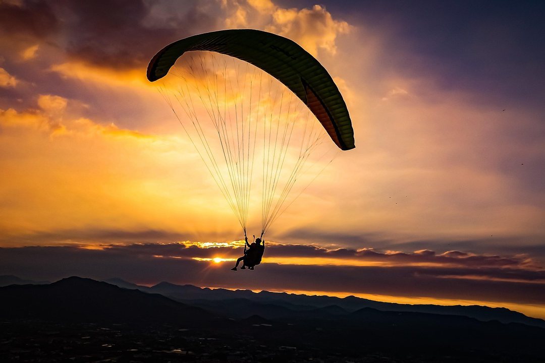Parachute canopy flying at sunset over mountains under a vivid orange sky