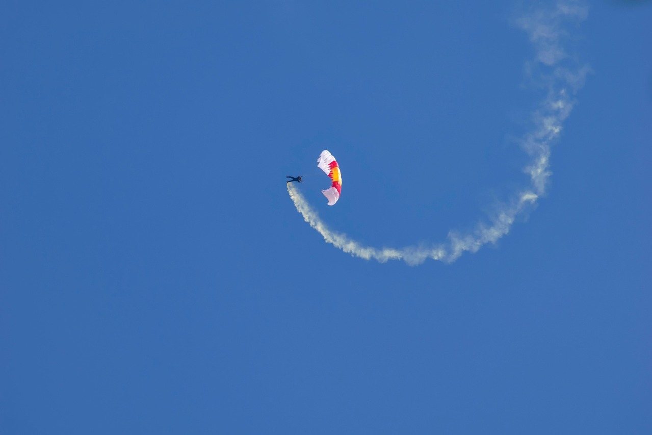 Parachutist performing aerial stunt with smoke trail against clear blue sky