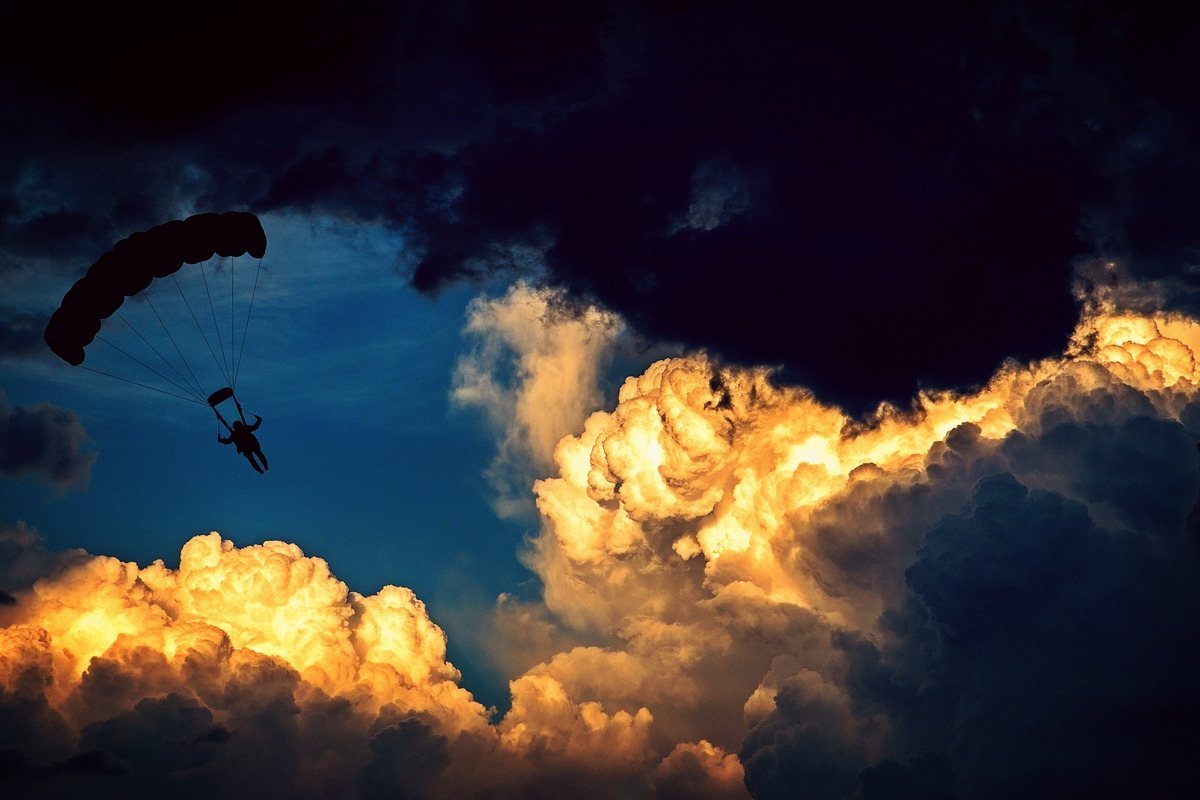 Parachutist descending through dramatic golden clouds at sunset