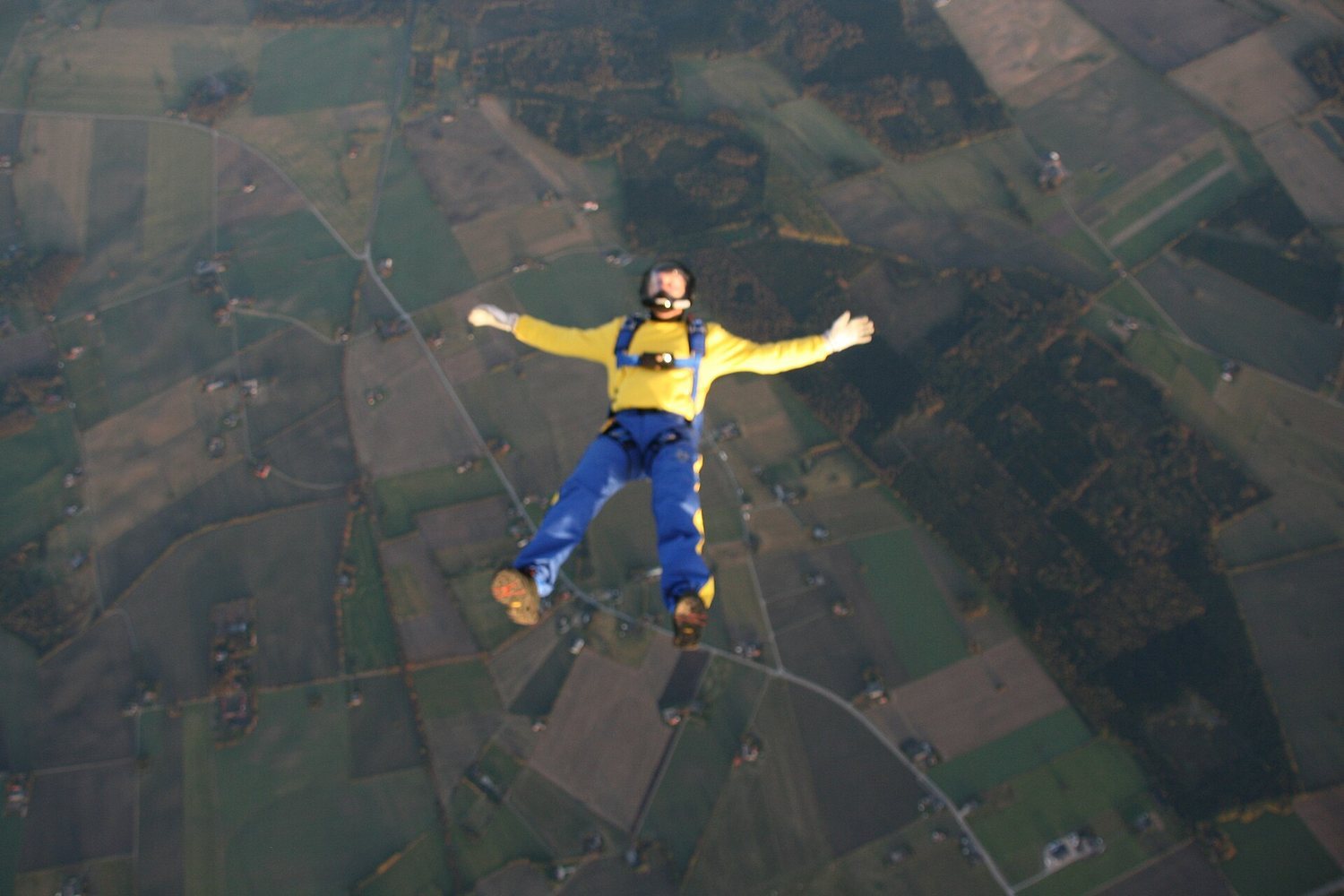 Skydiver in yellow jumpsuit freefalling over patchwork farmland below