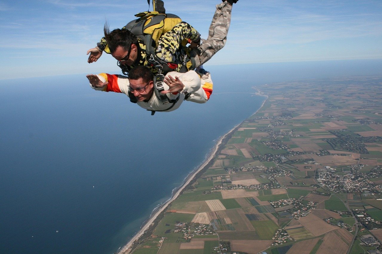 Two skydivers in freefall over coastal landscape with fields and ocean below