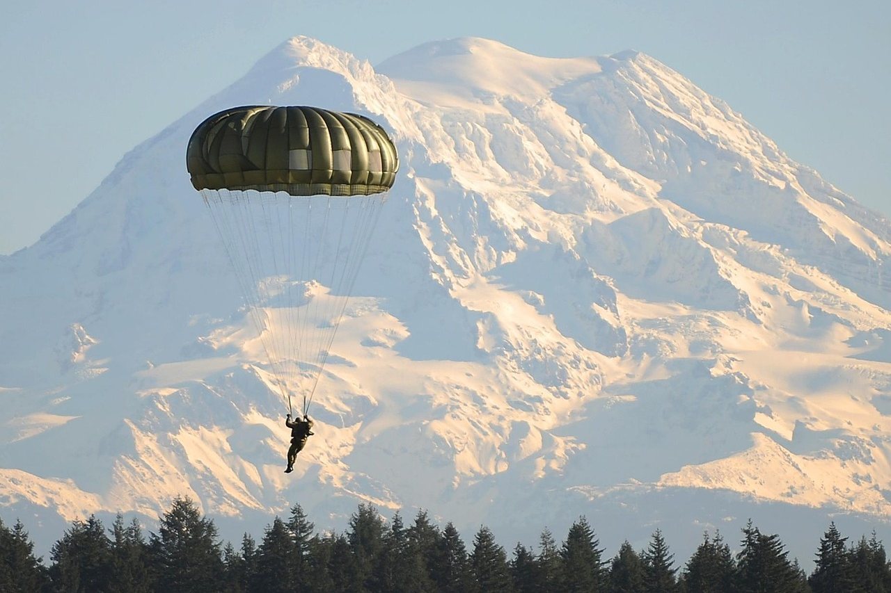 Paratrooper descending with parachute against snow-capped mountain backdrop