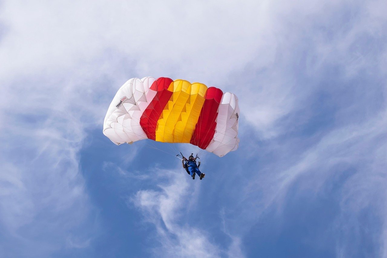 Parachutist soaring with red, yellow, and white canopy against blue sky
