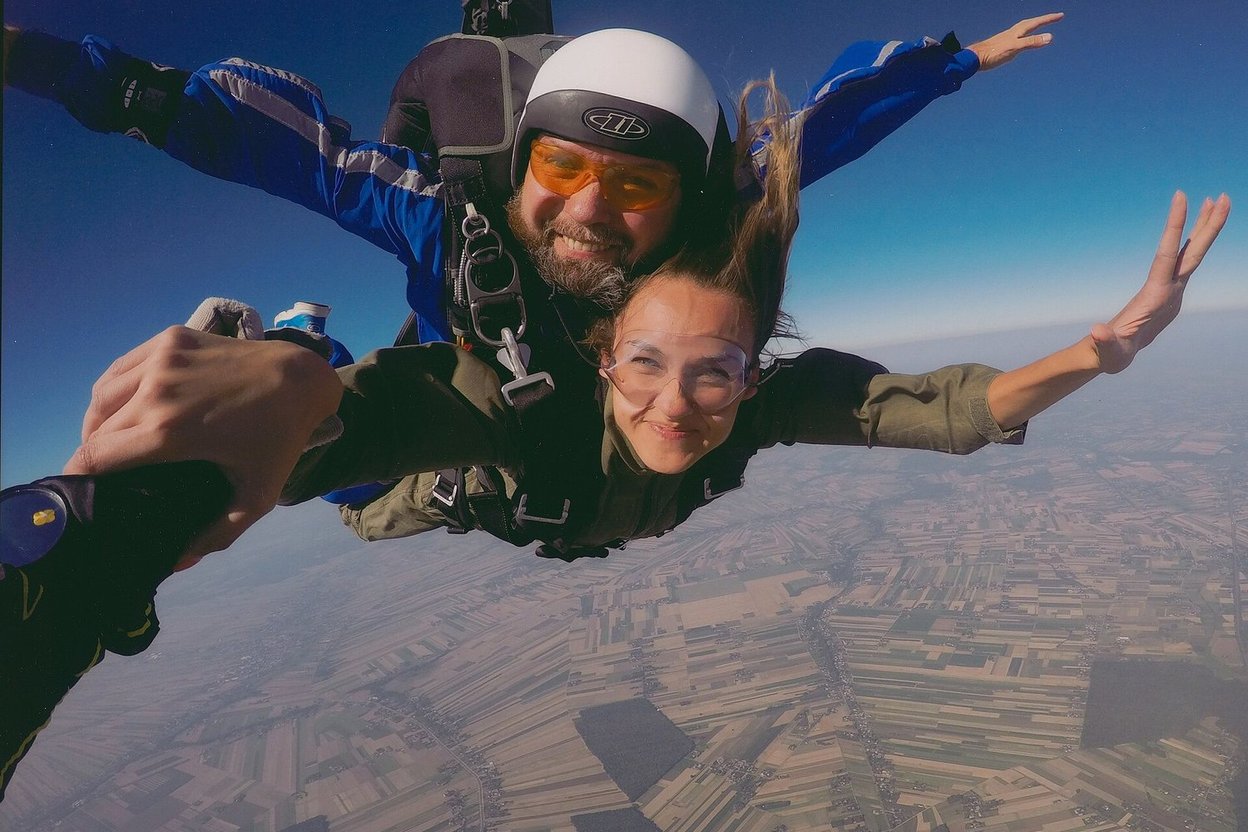 A tandem skydiving pair smiling in freefall above farm fields