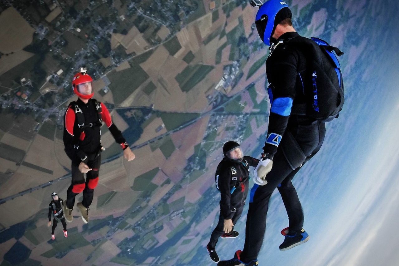 Four skydivers in freefall over a patchwork landscape below
