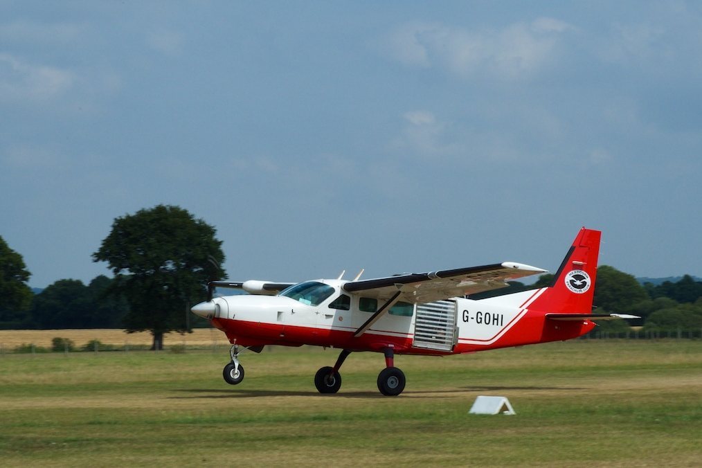 Red and white Cessna aircraft on grass runway with trees in background