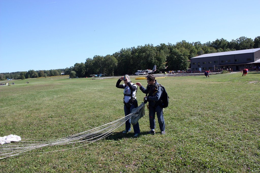 Two skydivers preparing their parachute on a grassy field near an airplane