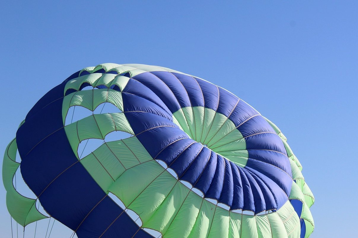 Blue and green parachute inflating against clear blue sky