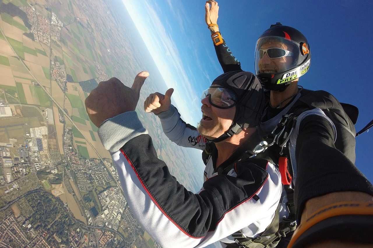 Two skydivers giving thumbs up mid-air over a patchwork landscape