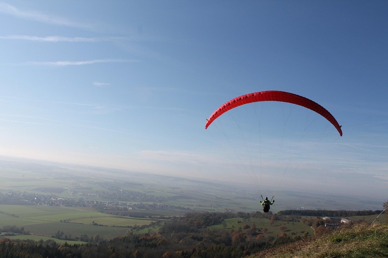 Red parachute canopy flying over a valley with green fields and trees