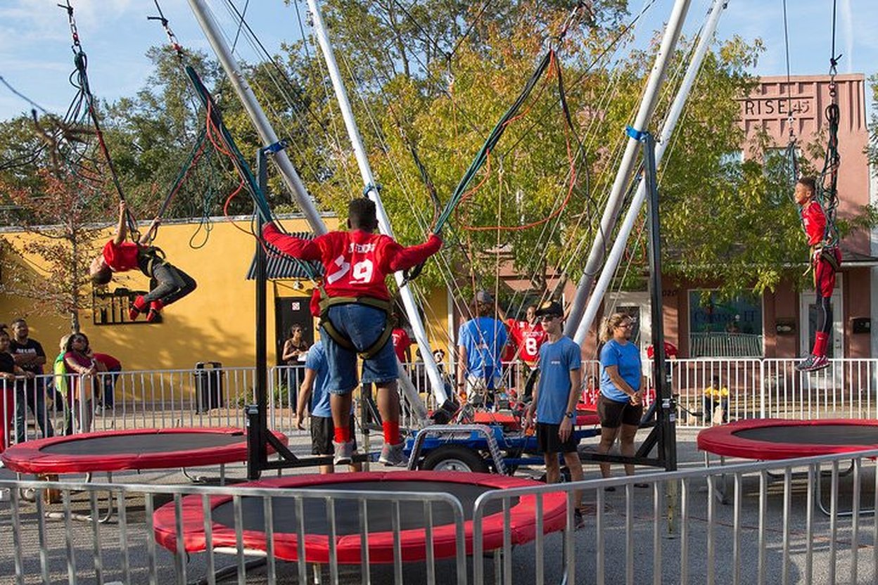 Kids in Halloween costumes jumping on trampolines at an indoor trampoline park with orange and black decorations