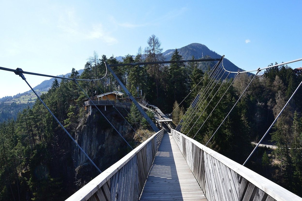 Bungee jump bridge spanning a forested valley with mountains behind it.
