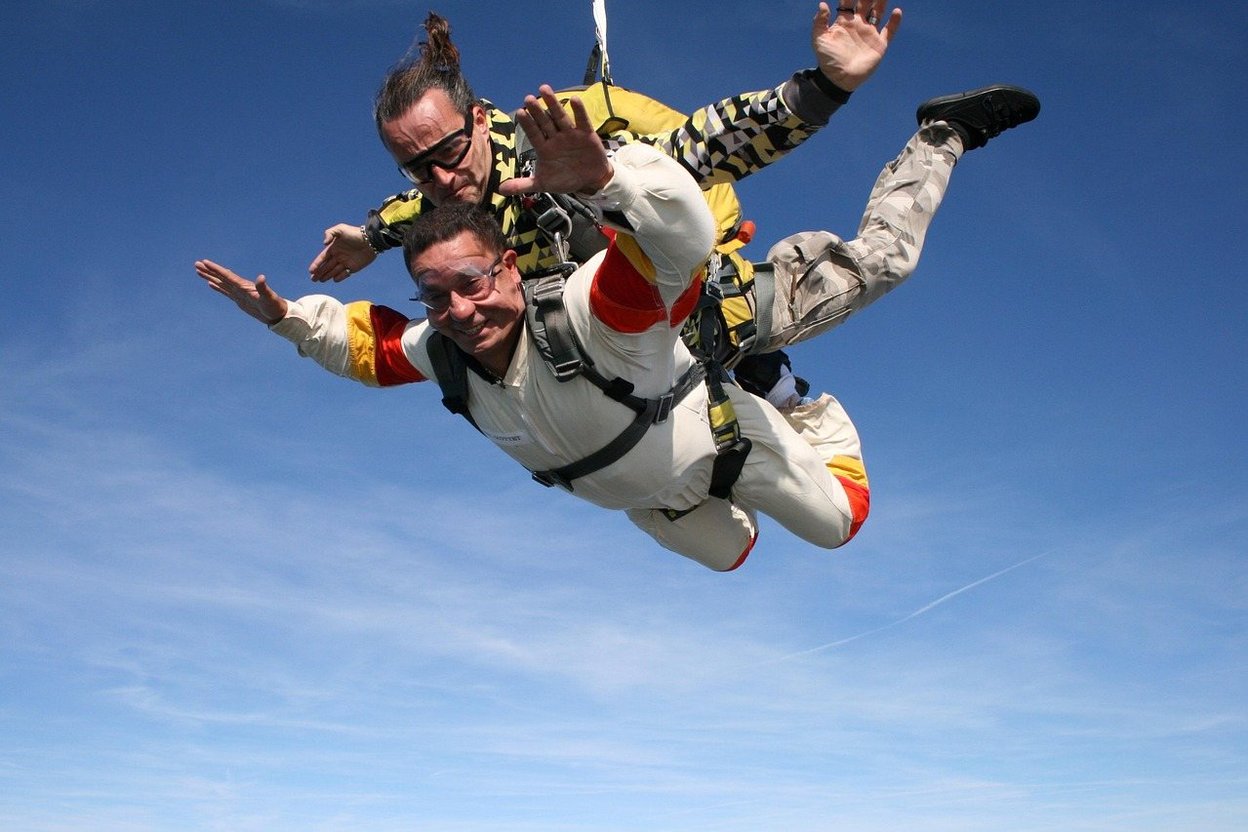 Tandem skydiver and instructor in freefall against a clear blue sky.