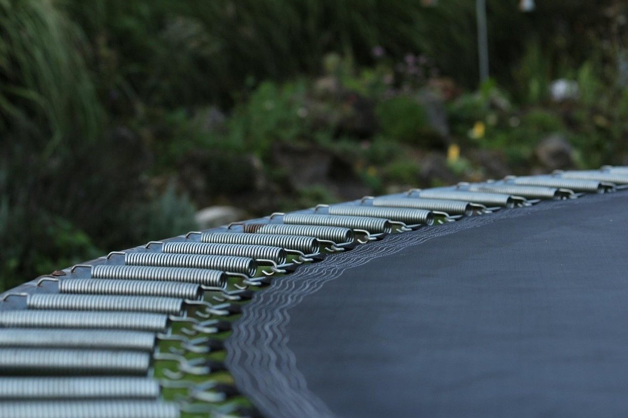 Close-up of trampoline springs hooked to the edge of a black jumping mat.