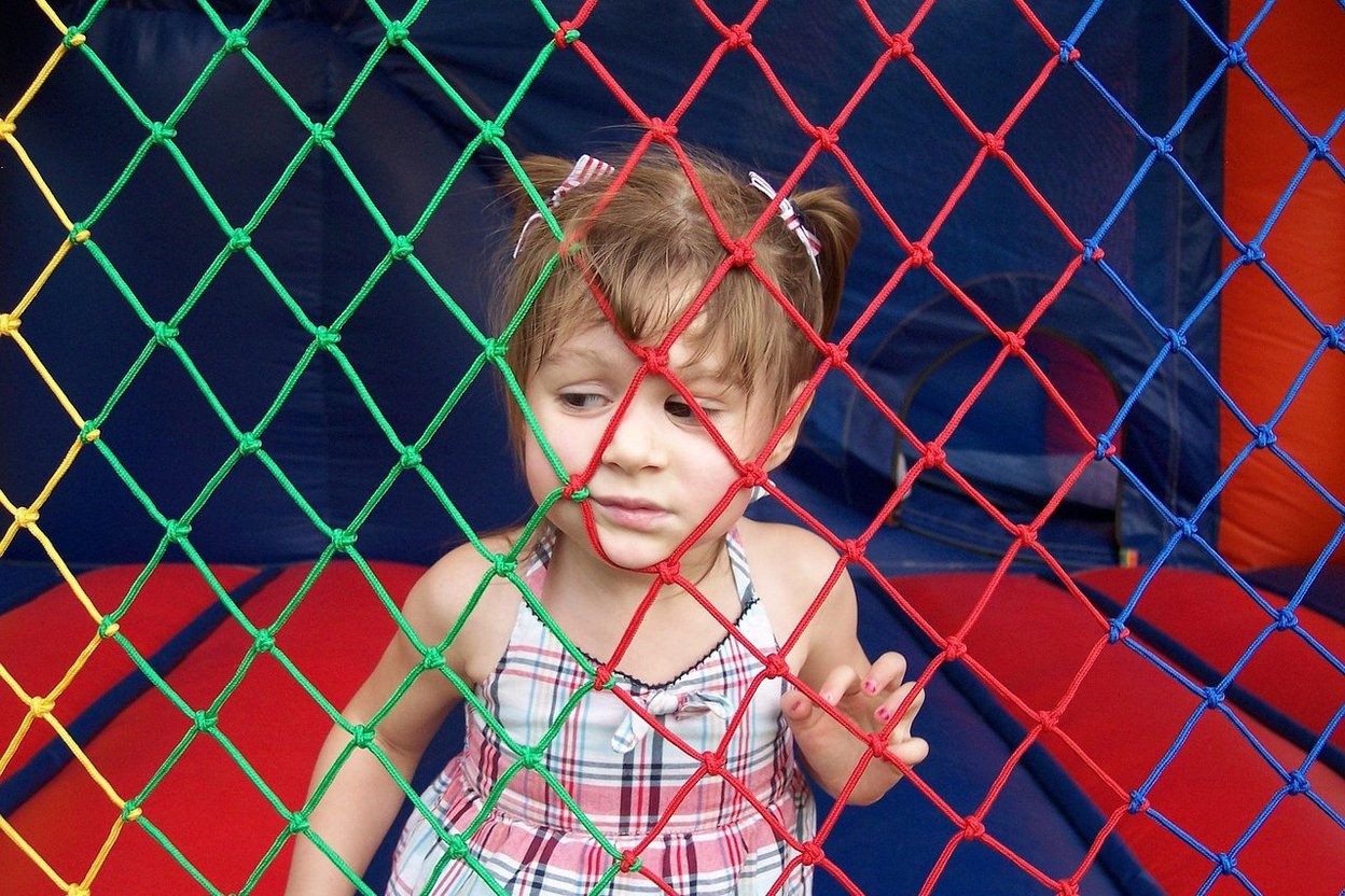 Little girl peeking through colorful netting at a play area.