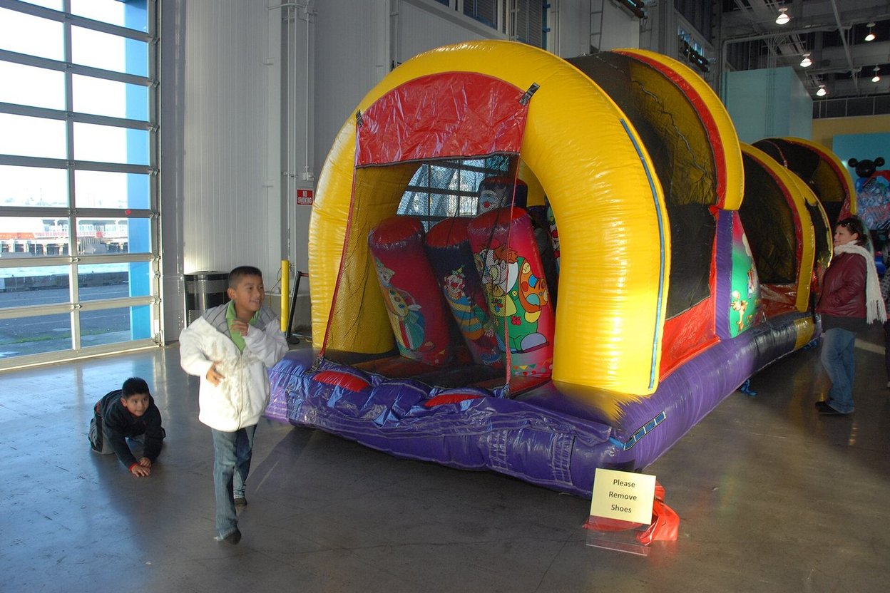 Children play near a colorful inflatable bounce house indoors.
