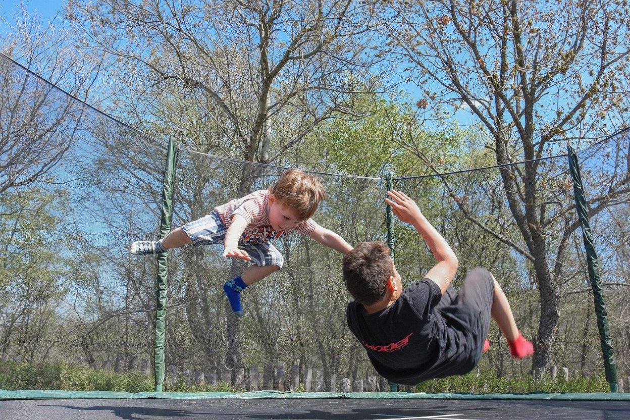 Two children mid-air on a trampoline, reaching toward each other.